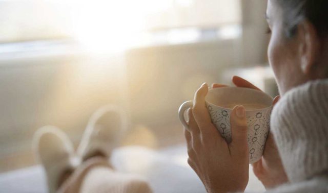 Woman enjoying a warm drink indoors on a bright winter morning.