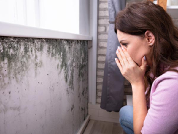 Woman looking at home's wall with mold damage.